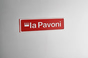 La Pavoni Cellini Classic Traditional Model logo, featuring a red rectangular nameplate with white text and crown symbol against a neutral gray background, showcasing the iconic Italian espresso machine brand's signature emblem